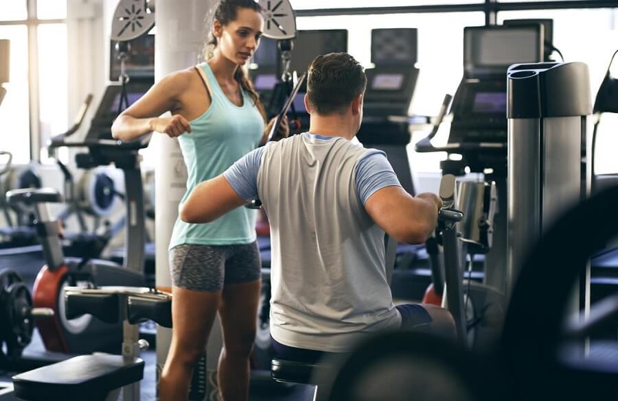 Un homme accompagné par une coach pour faire du rameur