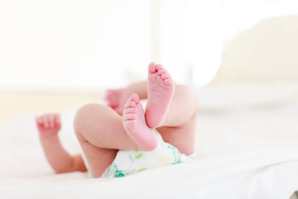 Jeune enfant qui dort sur un lit blanc, bébé dont on voit les pieds