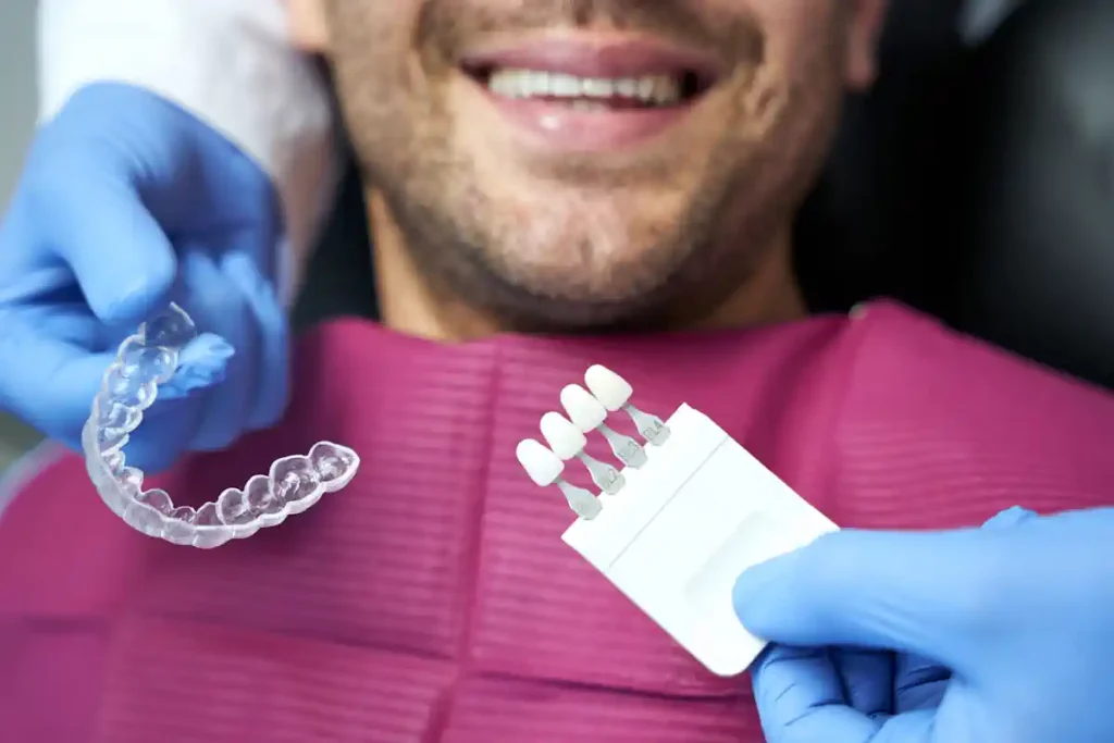 Un homme qui sourit entre les mains d'un dentiste qui tient des prothèses de dents blanches et une gouttière