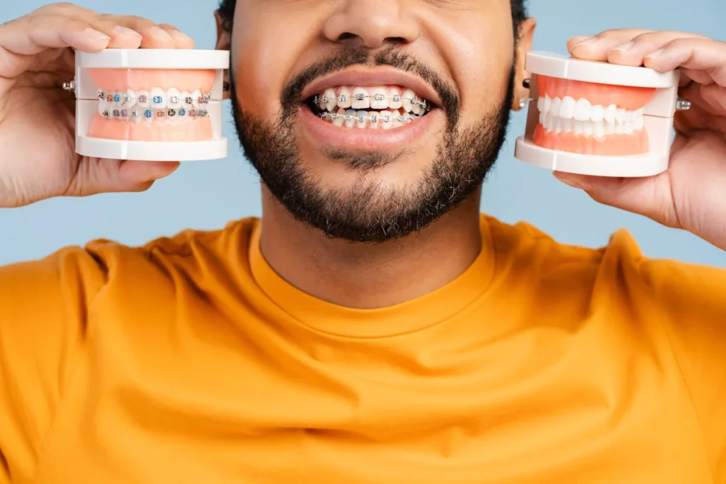 Un homme qui porteun appareil dentaire qui tient des prothèses dentaires avec et sans appareil dans ses mains