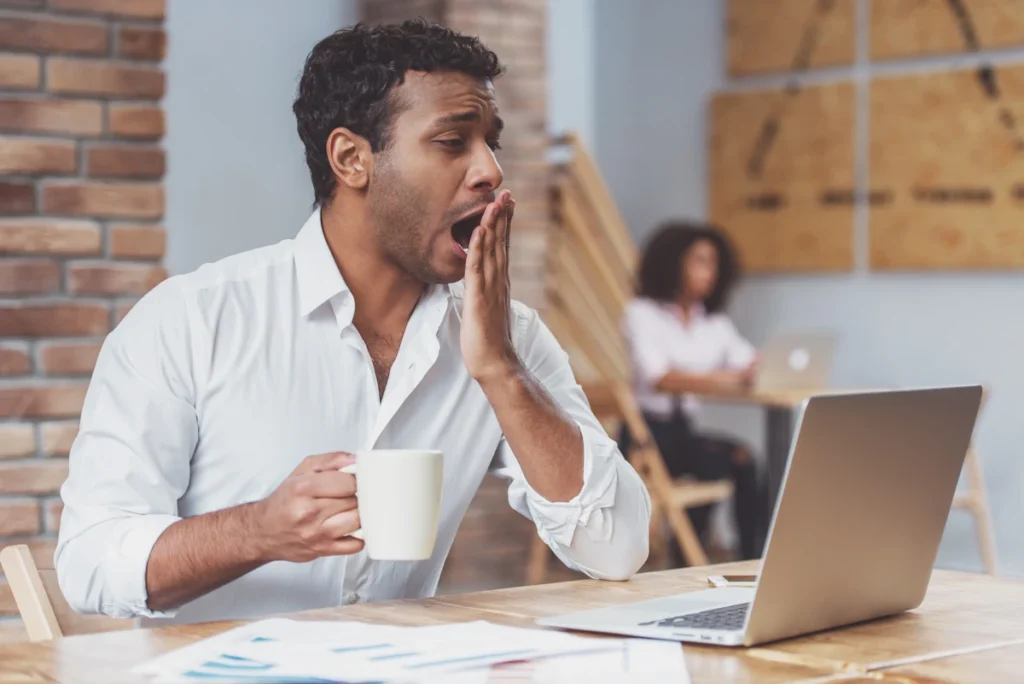 Un homme qui baille devant son ordinateur en tenant une tasse blanche dans sa main