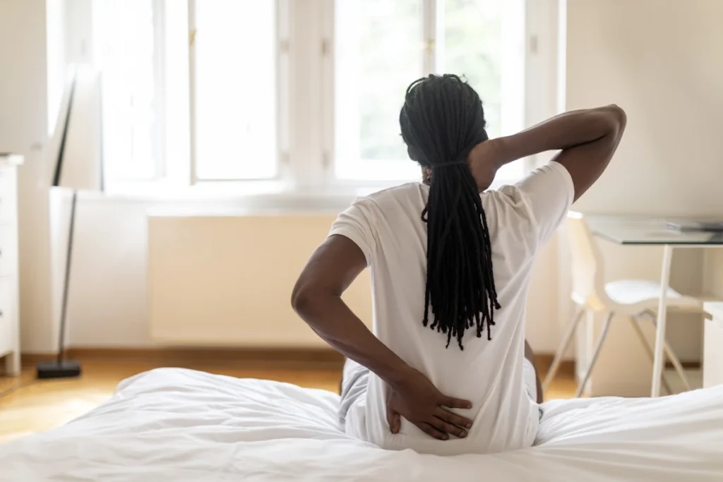 Une personne assise sur un lit qui se tient le haut et le bas du dos