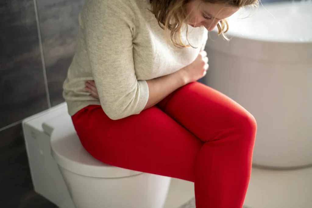 Une femme qui se tient le ventre étant assise sur les toilettes