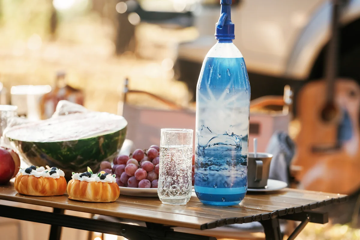 Une bouteille et un verre d'eau gazeuse posées sur une table où sont posés des fruits