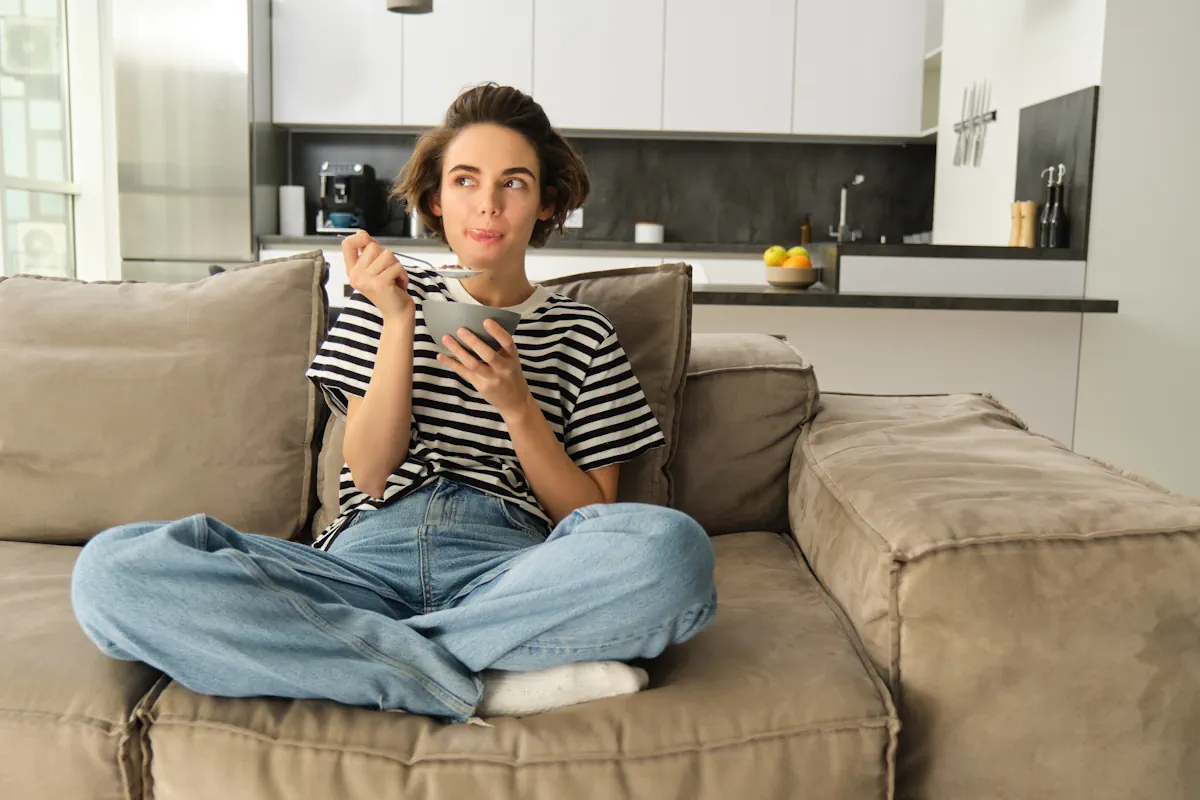 Une femme assise dans son canapé en mangeant une glace