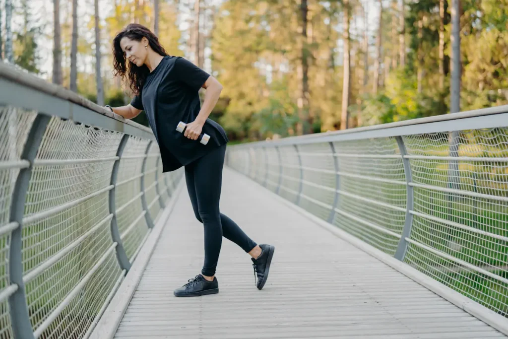 Une femme en tenue de sport noir qui s'appuie contre la rambarde d'un pont en tenant un poids dans la main