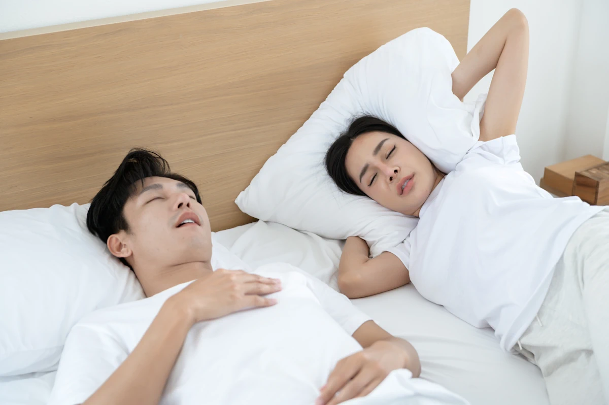 Une femme qui se bouche les oreilles avec un oreiller à côté d'un homme qui ronfle