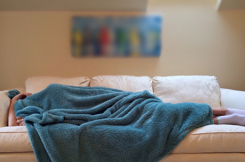 personne qui dort sur le canapé sous un plaid