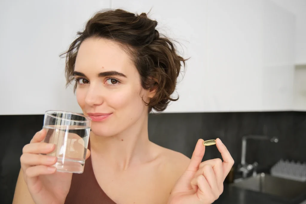 Une femme qui tient une gélule dans une main et un verre d'eau dans l'autre