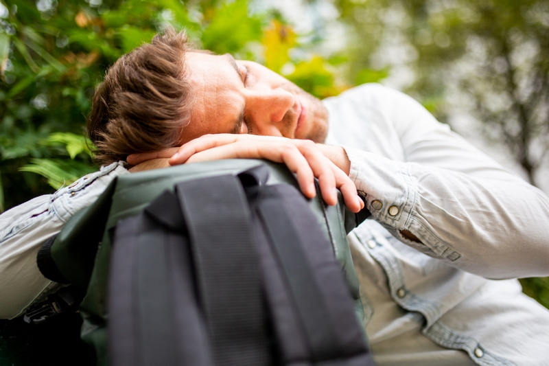 homme fatigué qui s'endort sur son sac