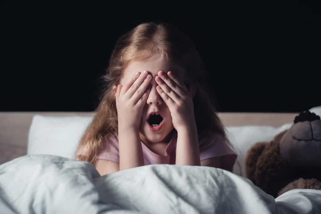 une petite fille dans on lit qui ne dort pas et qui se cache les yeux