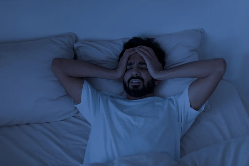 Un homme qui n'arrive pas à dormir et qui se tient la tête dans son lit