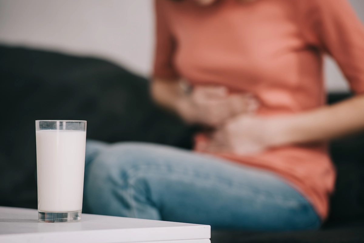 Une femme qui se tient le ventre assise devant un verre de probiotiques